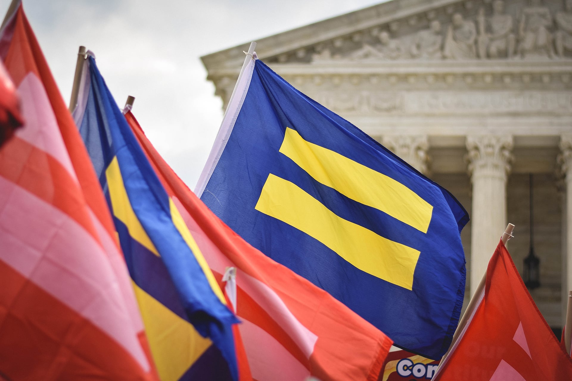 equality flag waving in front of a courthouse building with other flags